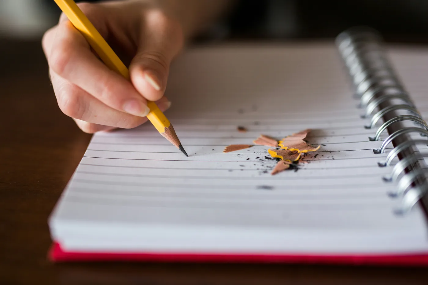 A hand writing in a spiral notebook with a sharpened pencil